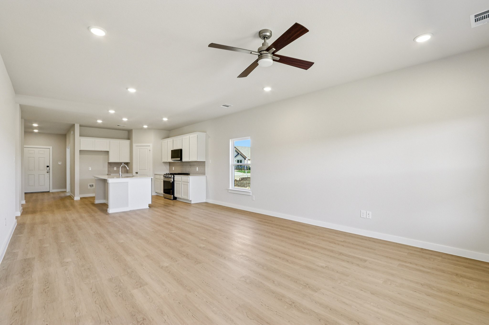 A large empty room with a ceiling fan and a wood floor.