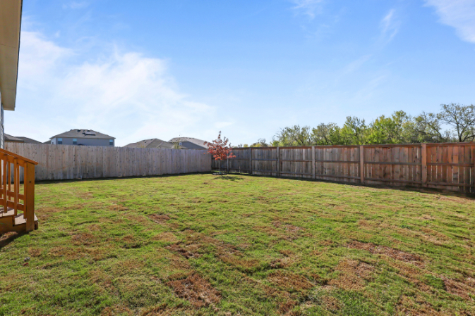 A fenced in yard with a wood fence and a building in the background.
