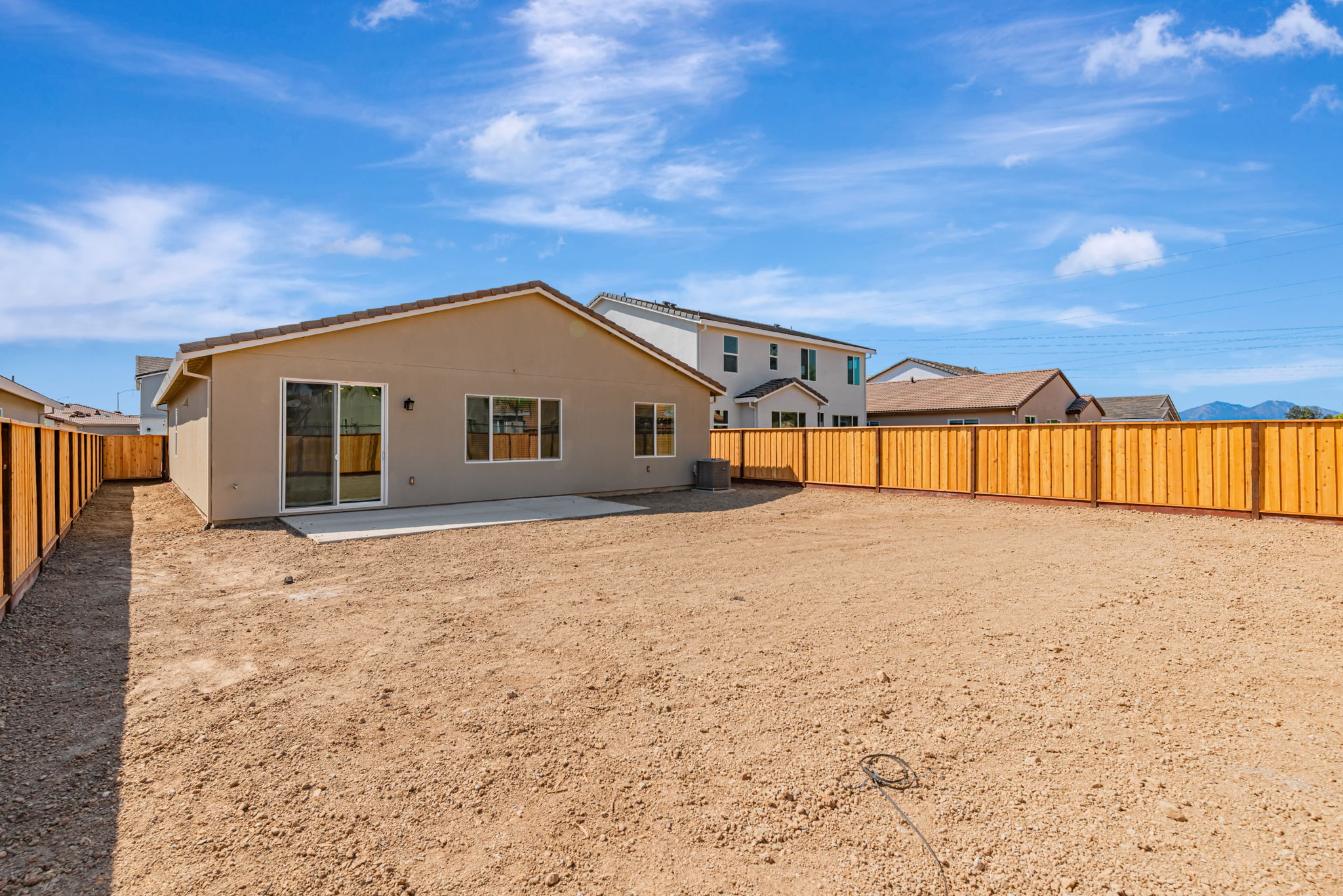 A dirt yard with a fence and a house in the background.
